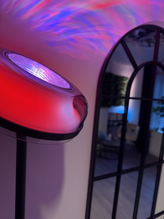 A light projector casting pink and blue patterns beside an arched mirror